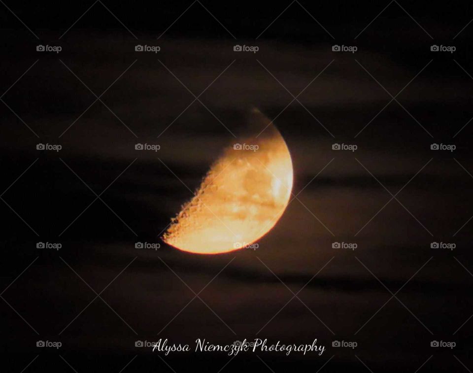 Orange moon phase. Clouds streak across creating a stunning view up above. Craters visible.