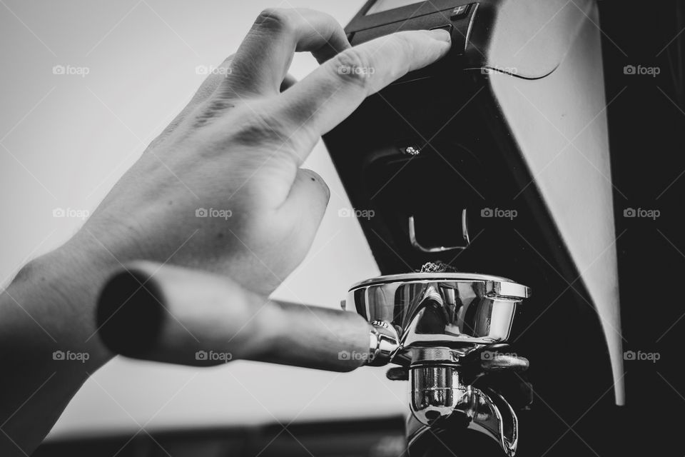 A black and white portrait of someone utilizing a coffee bean grinder with a portafilter holder. the coffee grounds will go straight into the portafilter.