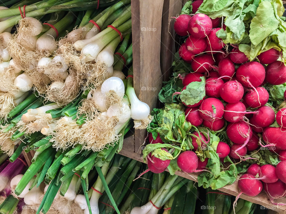 Bunches of fresh organic cultered white spring onions and red radishes in wooden box for sale at farmers market