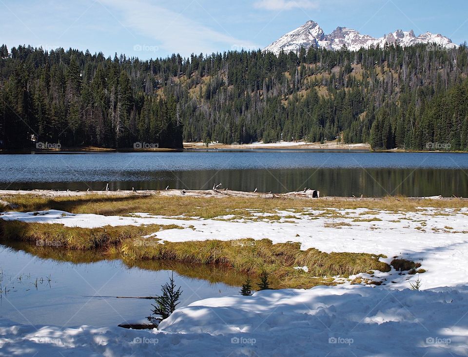 Todd Lake with Broken Top in the background with snow still on the ground in early summer on a sunny summer morning in the Cascade Lakes in Central Oregon.