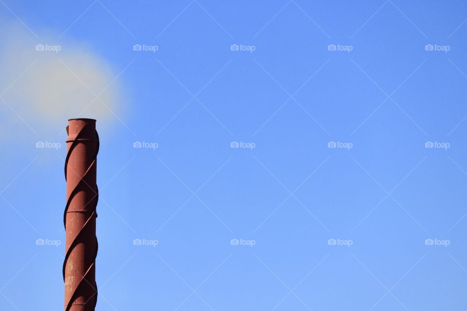 Pollution: large rusted steel industry tower blowing smoke into atmosphere clear vivid blue sky minimalist with negative space for text 