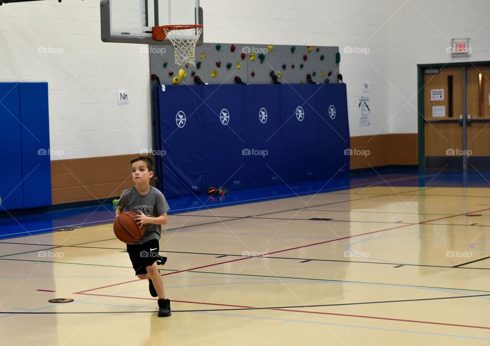 Young boy running down a basketball court while dribbling a basketball 