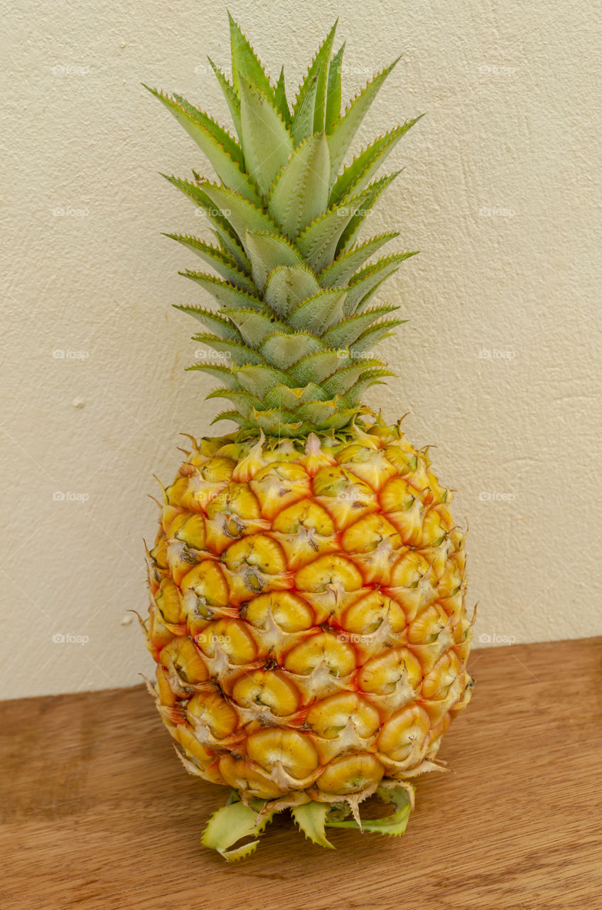 Yellow Ripe Pineapple fruit with green prickly top standing on a board surface.