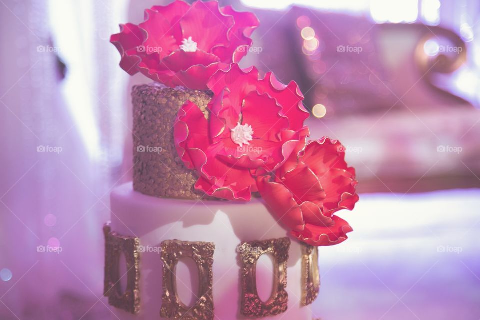 A fancy cake with massive pink flowers and decorated in gold