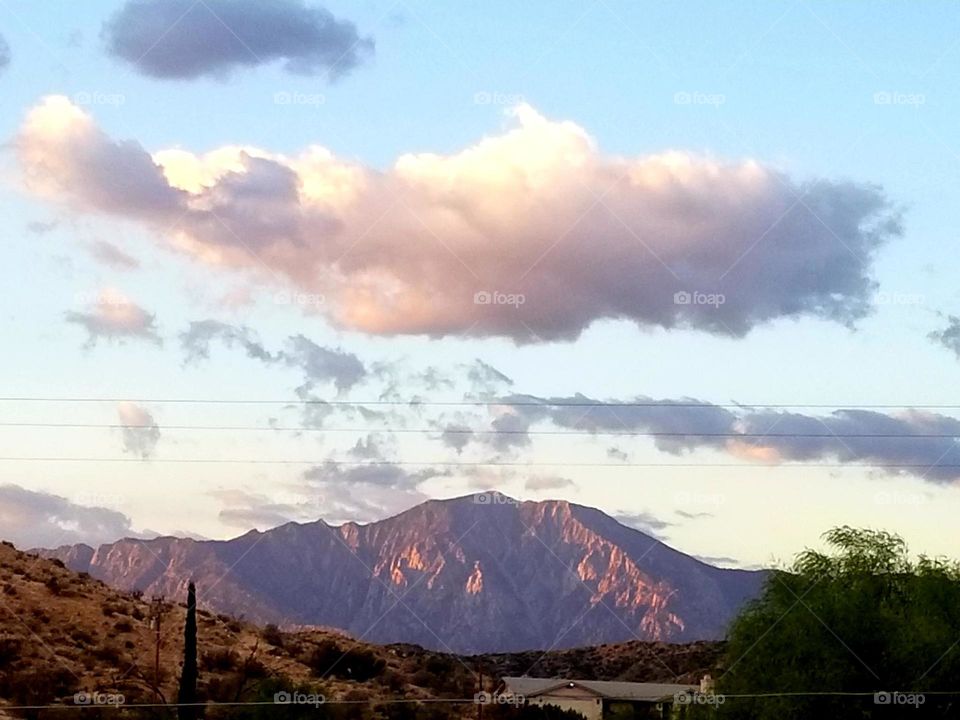 A pink glow is seen in the sky over the mountain as the sun sinks below the horizon. Evening Stories.