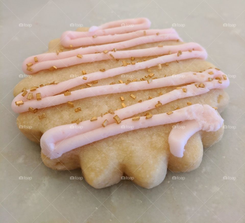 Shortbread cookie decorated with pink icing and gold sprinkles