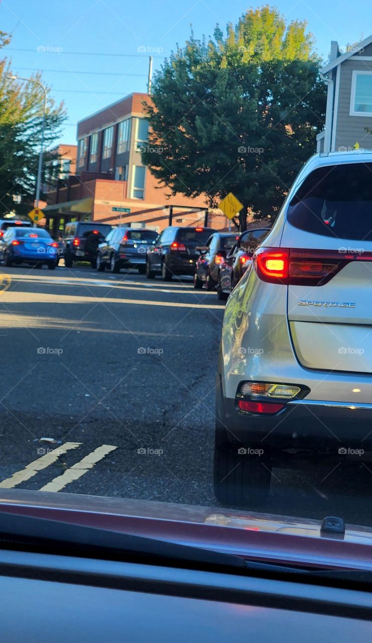 long line of cars with red tail lights waiting at a traffic light in an Oregon neighborhood during rush hour