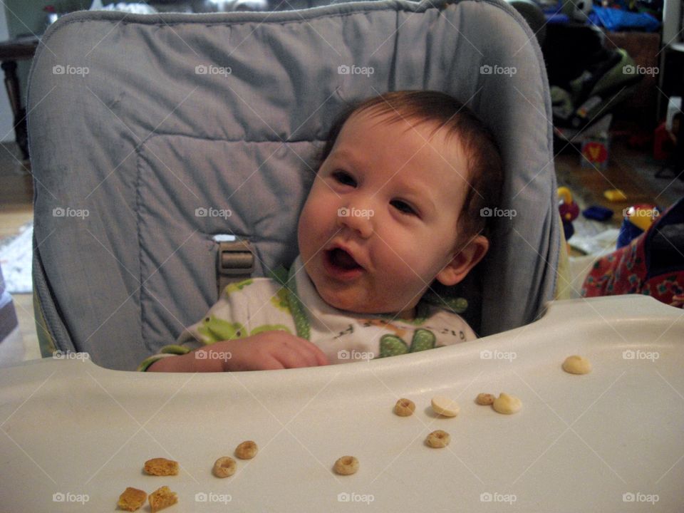 Young Child Learning To Eat Solid Food In A High Chair