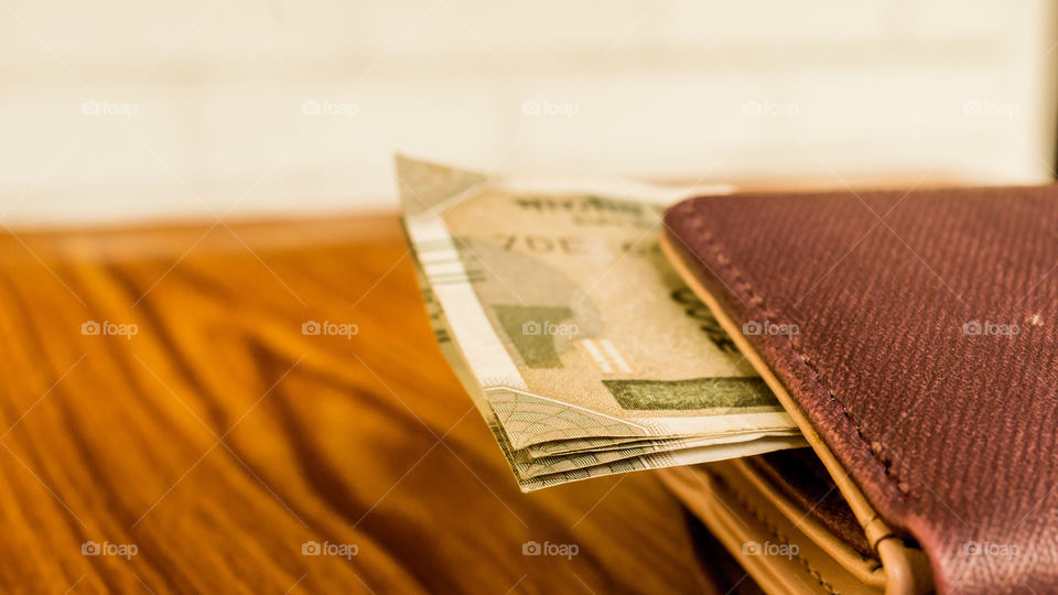 Indian five hundred (500) rupee cash note in brown color wallet leather purse on a wooden table. Business finance economy concept. Side angel view extreme close up with copy space room for text on left