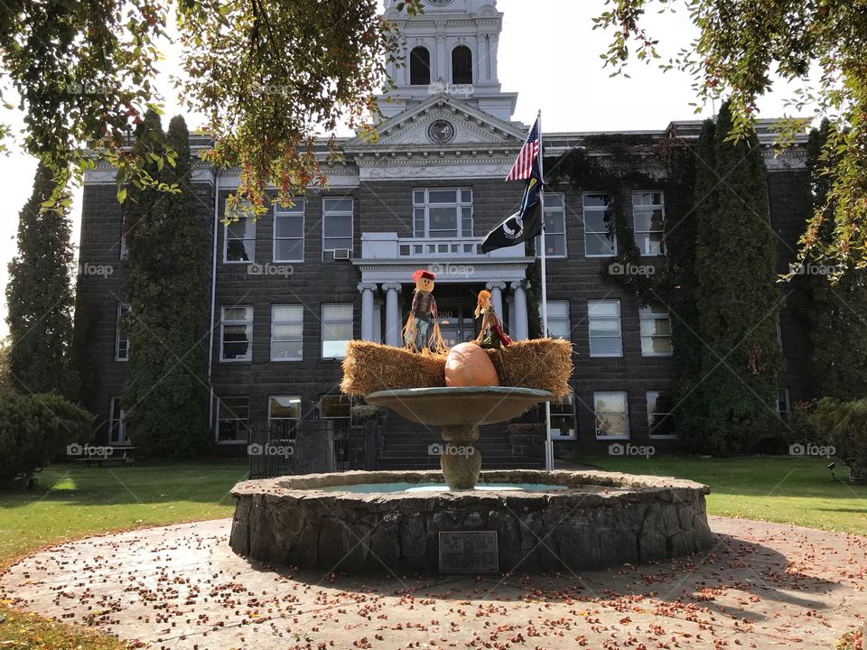 A pair of decorative scarecrows perched on hay bales with a pumpkin in the fountain at the old Crook County Courthouse in Prineville in Central Oregon on a beautiful fall day. 