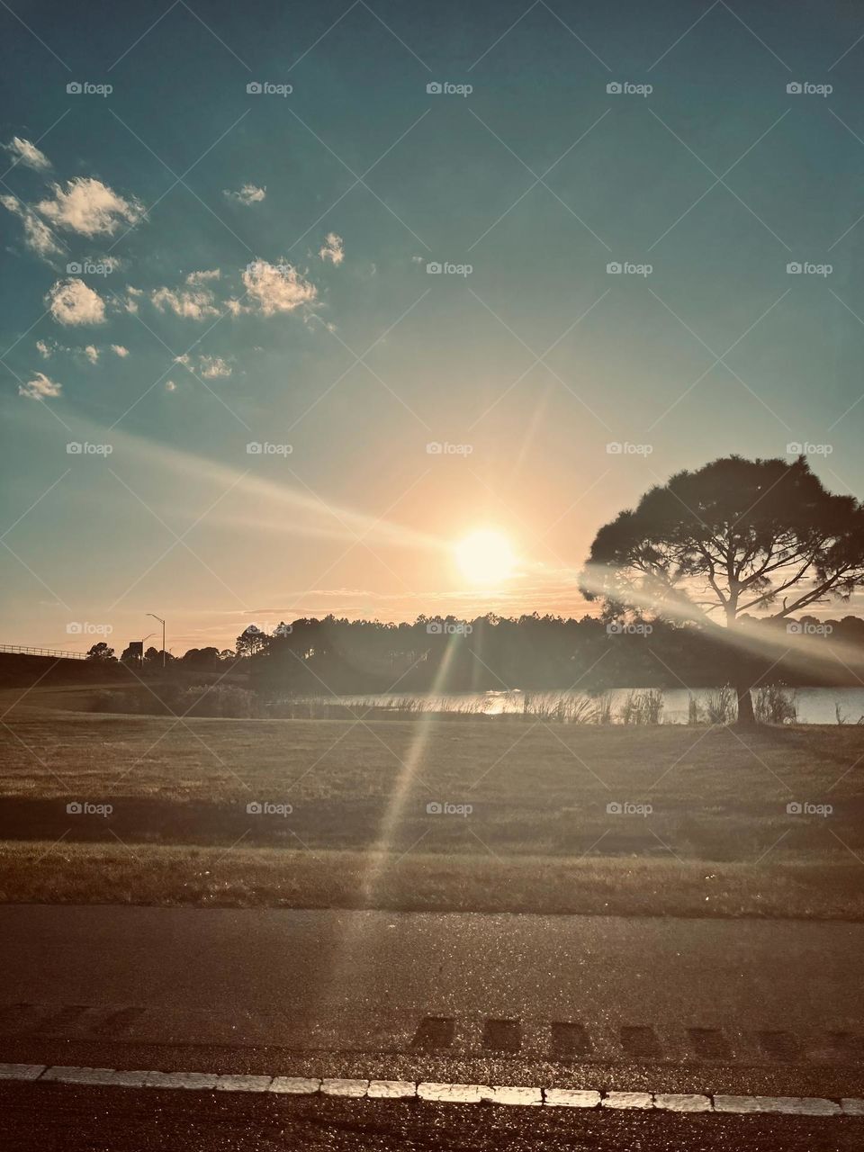 Sunrise With Sun Rays By A Body Of Water In A Tropical Environment Showing The Beauty Of The Creation With Reflection On The Water With Trees By The Road.