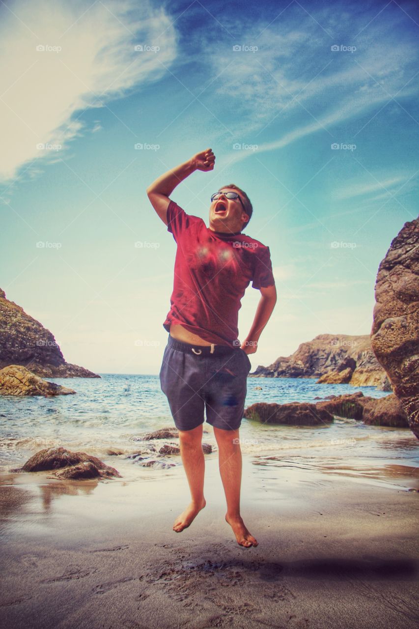 Jump For Joy. A boy on a sandy Cornish Beach jumps for joy with the ocean behind him. Kynance Cove in Cornwall