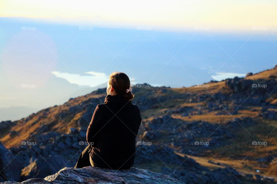 looking valley. woman sitting looking valley from edge at sunset