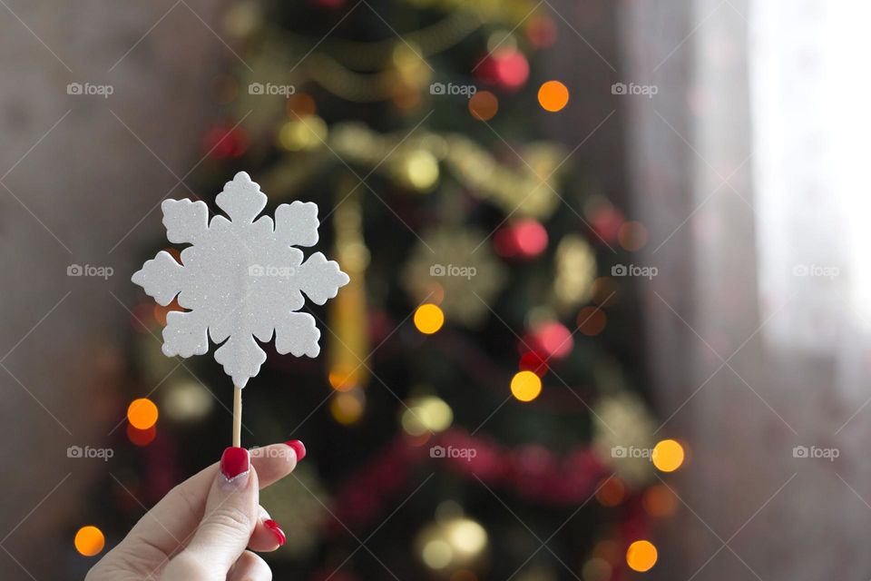 Female hand holds paper snowflake on the Christmas tree background 