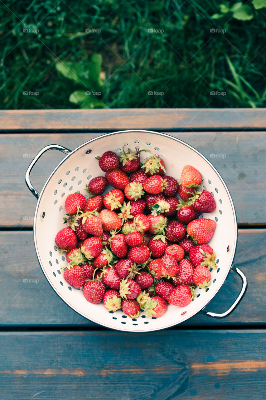 Closeup of bowl of fresh strawberries sprinkled raindrops on wooden table