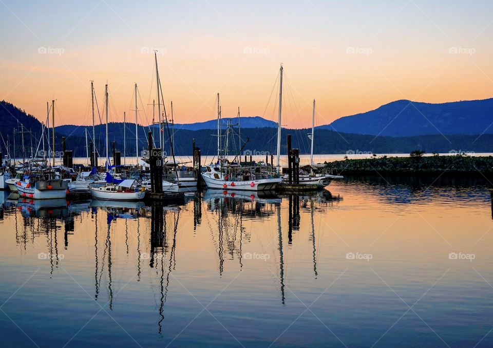 Sailboats reflect on ocean under a scenic setting sun