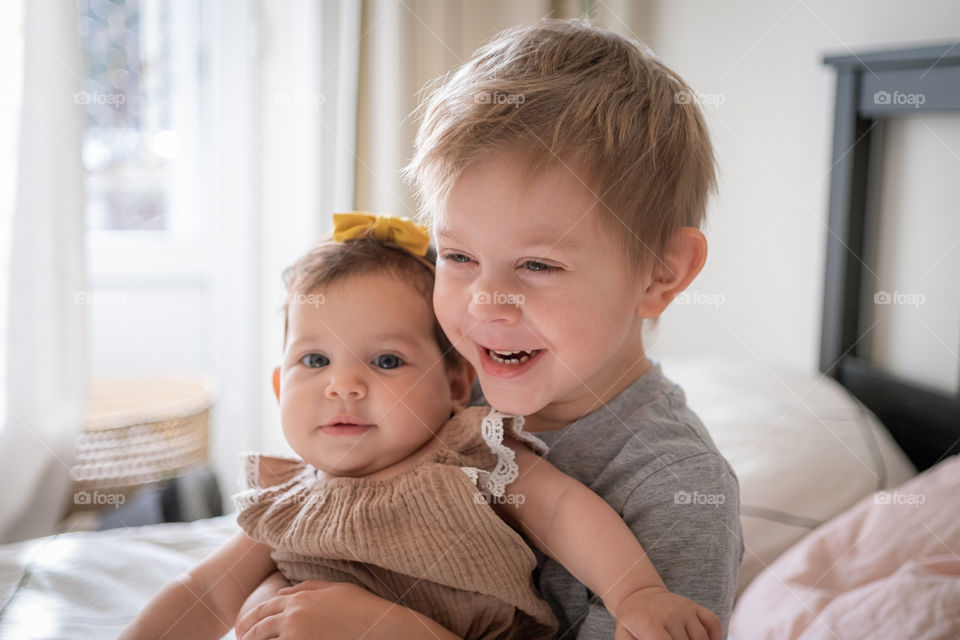 Toddler boy embarrassing his infant sister and laughing 