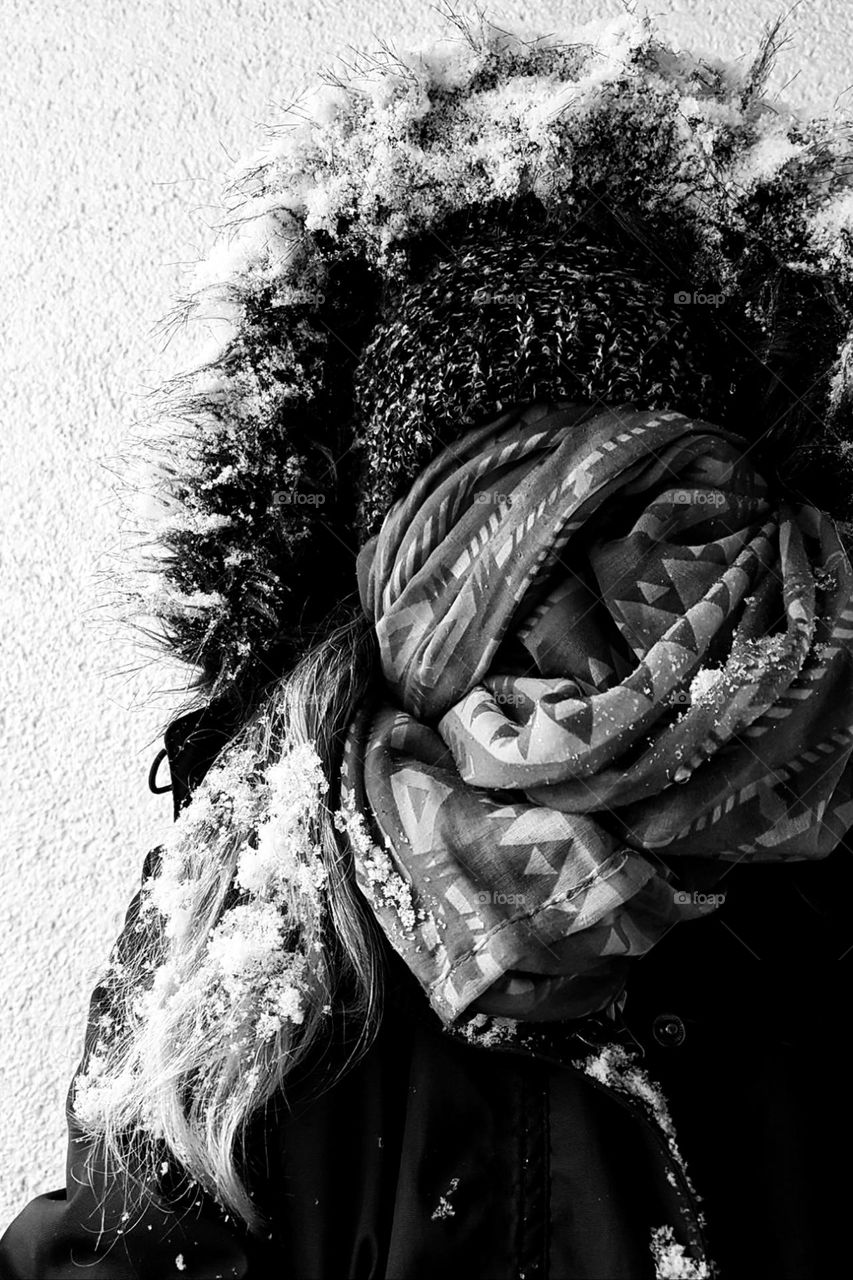 Black and white photo of a woman with long hair wrapped in scarf and hat covered in snow after a snowstorm 