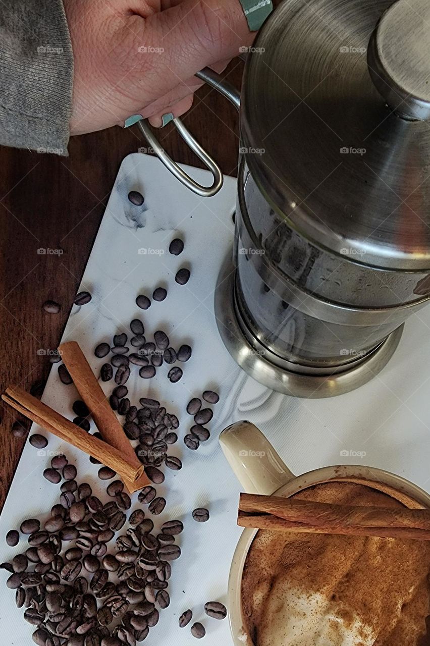 French press coffee maker with scattered coffee beans and cinnamon sticks.