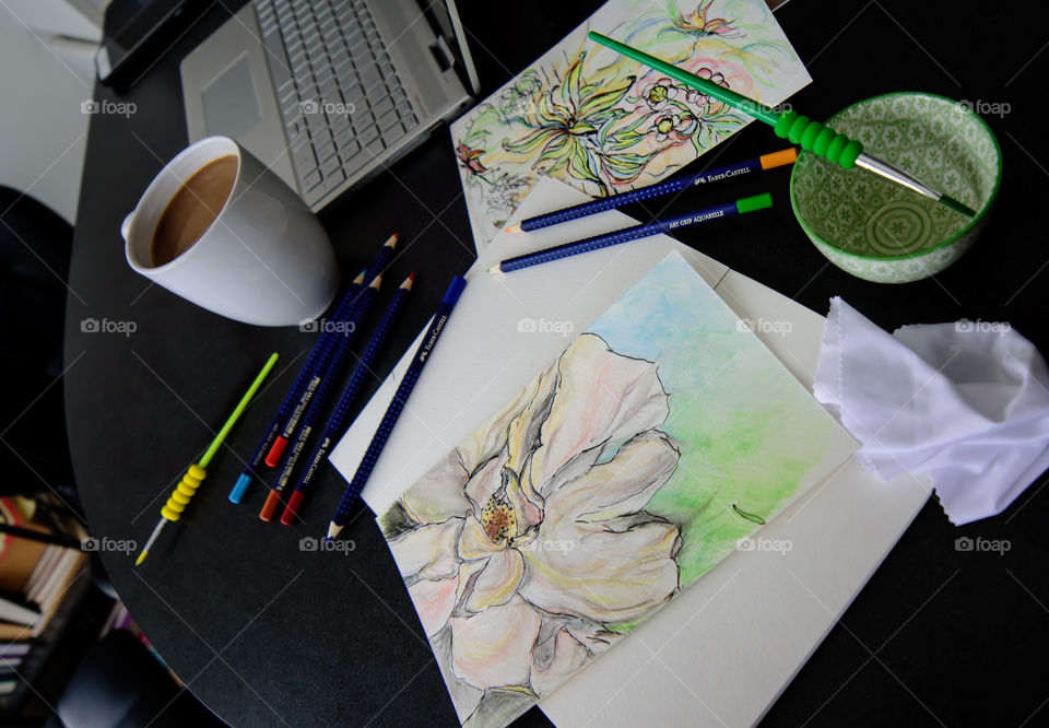 High angle view of Desk with Floral spring creative sketches, coffee, laptop and art tools Sketching with Faber-Castell PITT Artist pens and aquarelle pencils using watercolor techniques