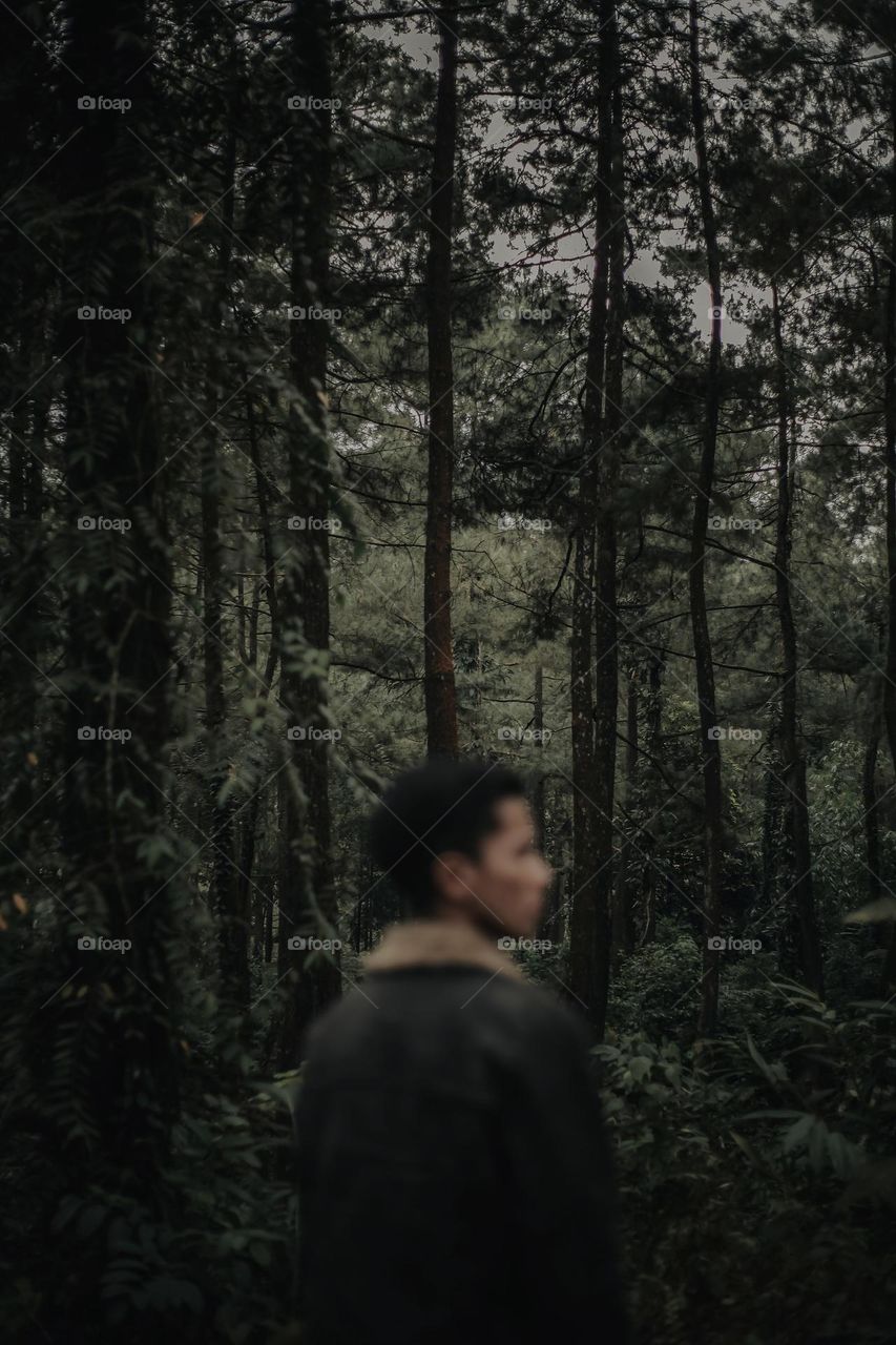 man standing looking sideways in the middle of the forest