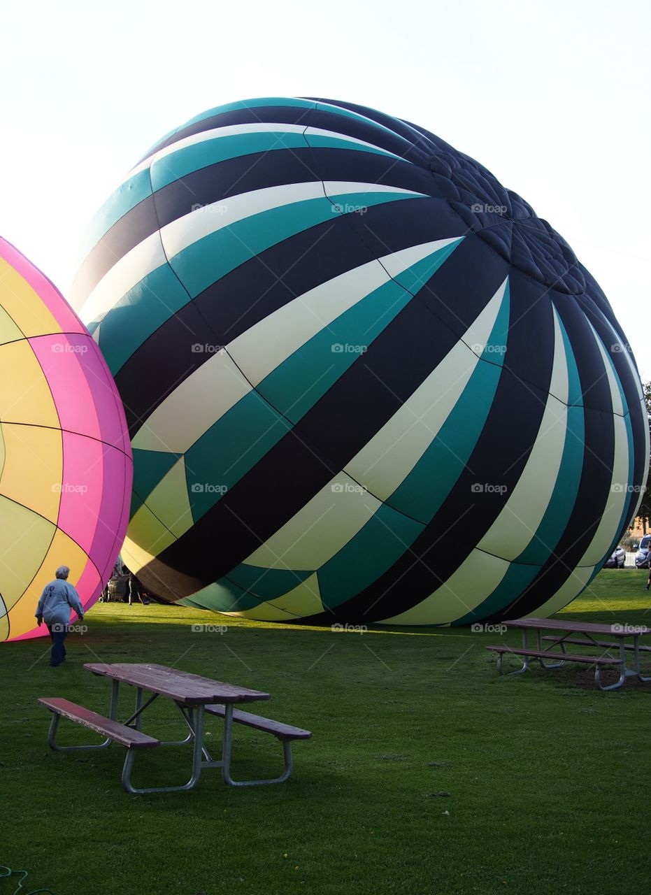 Two bright and colorful hot air balloons on the grass of Ochoco Park filling with helium for a morning flight over Prineville in Central Oregon on a beautiful summer morning as the sun rises.