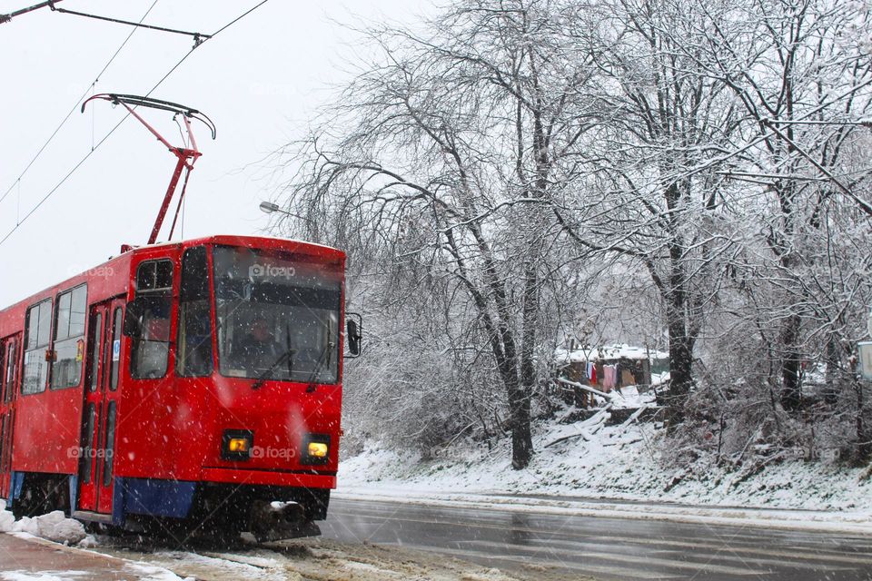 Winter landscape in the city.  While the snow is falling and old red tram slides down the street