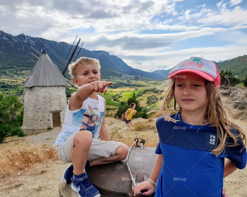 two children on a hill with wiew over mountains and an old windmill in the background.