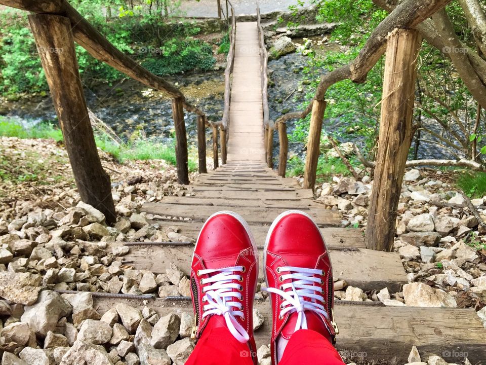 Women red sneakers with white laces on the steps of a wooden bridge