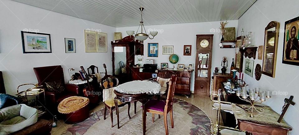 This is the living room of the one story house in “Bavaria”, Germany. It has been filled with antique as well as new furniture, an old stand up clock, tables and chairs to accommodate for get togethers and musical soirées. 2023. Hypnotic Productions