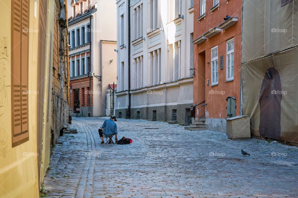 A lonely street painter sitting on a chair in an empty alley in Riga, Latvia