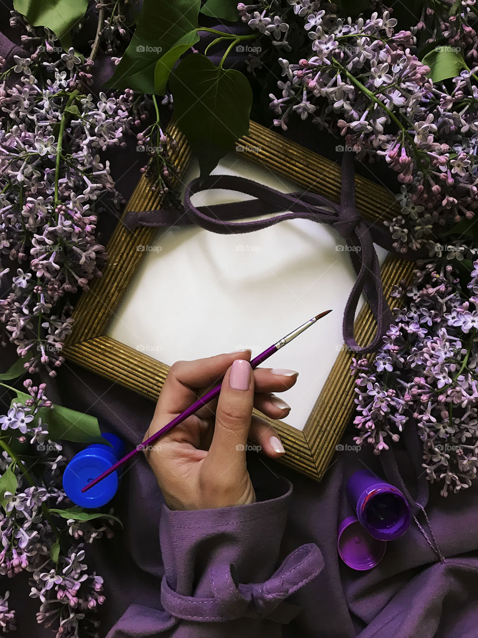 Female hand Drawing at empty frame by purple paints among the lilac flowers 