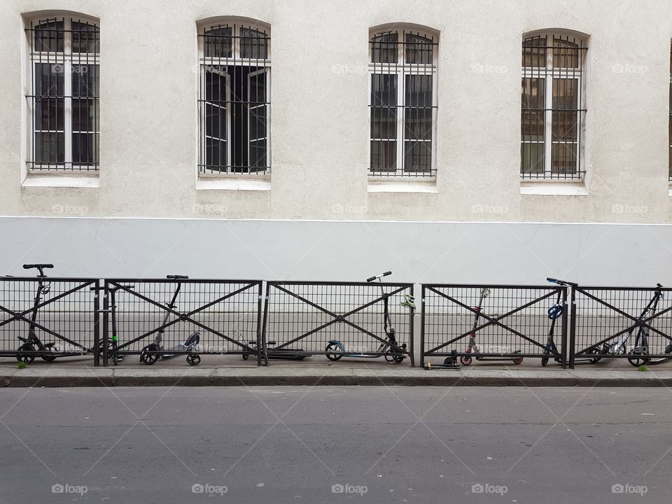 Row of parked children's scooter next to a school in Paris on the sidewalk