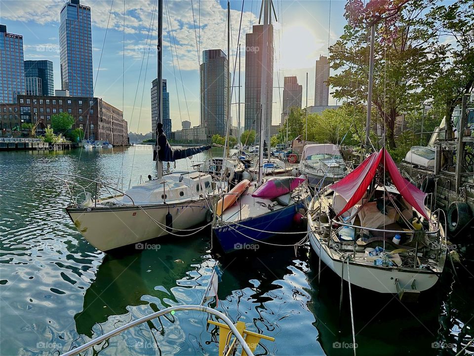 In the warm golden glow of the evening sun we see various sailboats at “Newtown Creek” from aboard “Salvation”, a “28 foot 1969 Luhrs” cabin cruiser by the “Pulaski Bridge” in LIC, Queens. 2024. Hypnotic Productions