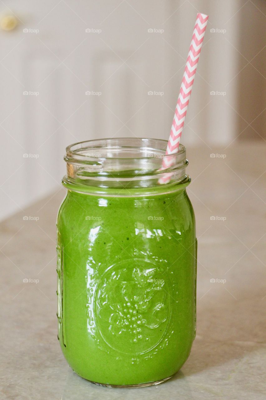 Green Smoothie Juice with Pink and White Paper Straw in Kitchen