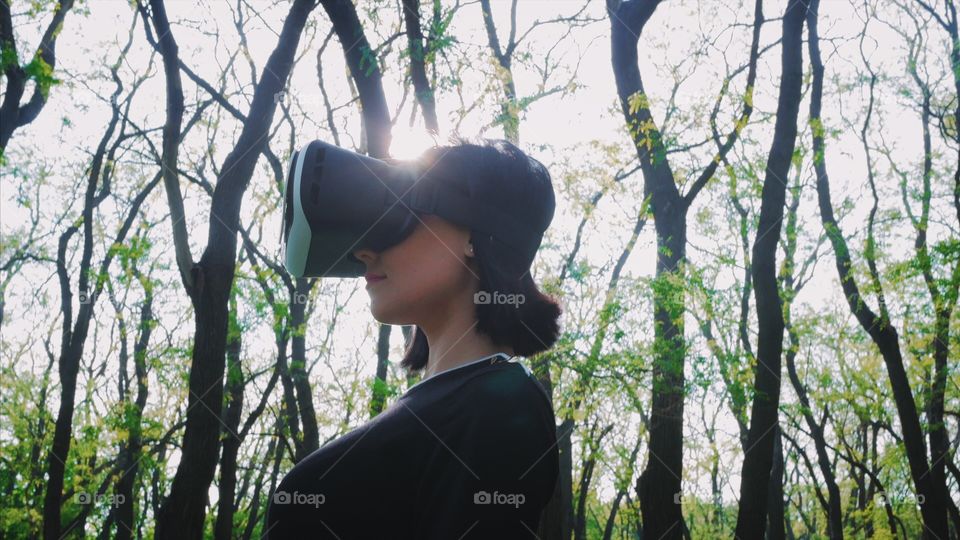 Portrait of trendy woman  using virtual reality glasses simulator in the park or forest at spring 