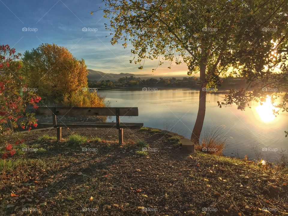 View of bench by lake during sunrise