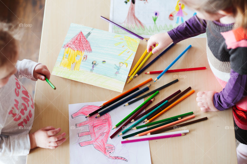 Little girls drawing a colorful pictures of elephant and playing children using pencil crayons standing at table indoors. Shot from above