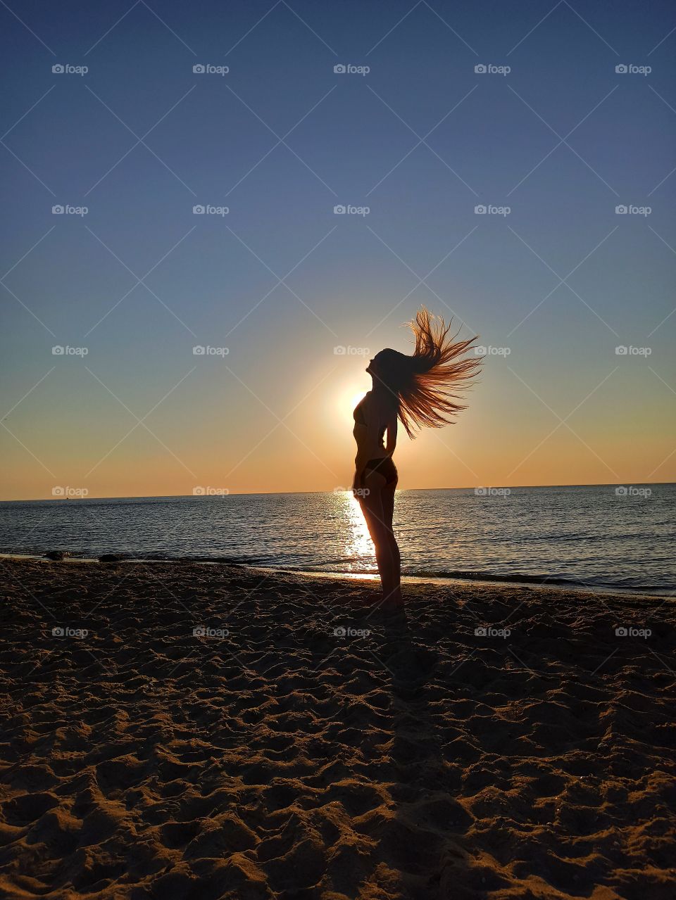 The girl waves her hair at dawn on the coast of the sea. Dawn. Silhouette of a girl. Silhouette. Hair. Shine. The sun. Sea. Sunrise.