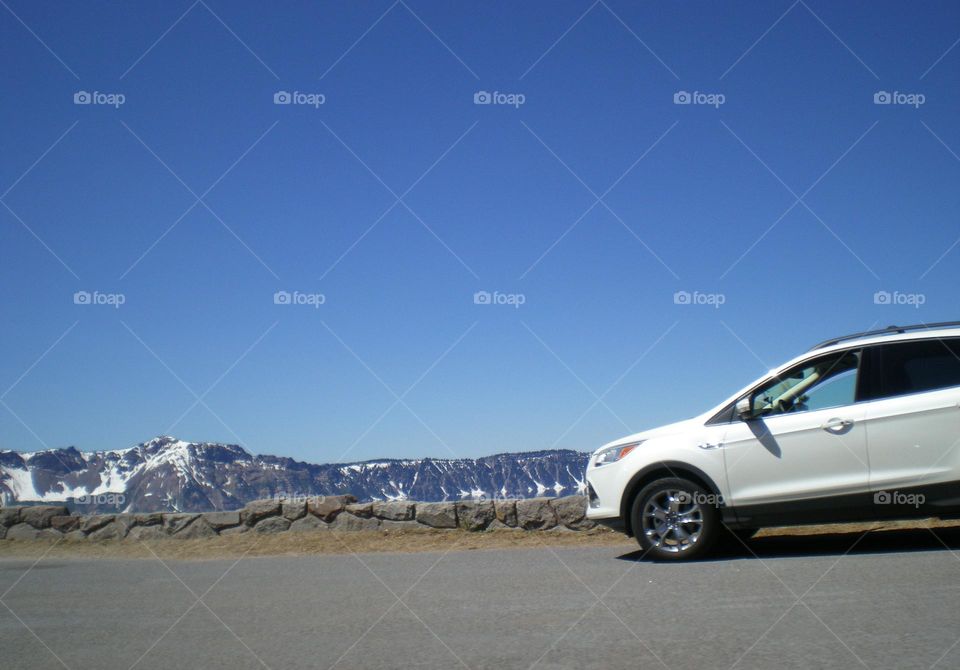 white Ford Escape car parked by rocky overlook at the edge of Crater Lake on a clear blue sky day in Oregon