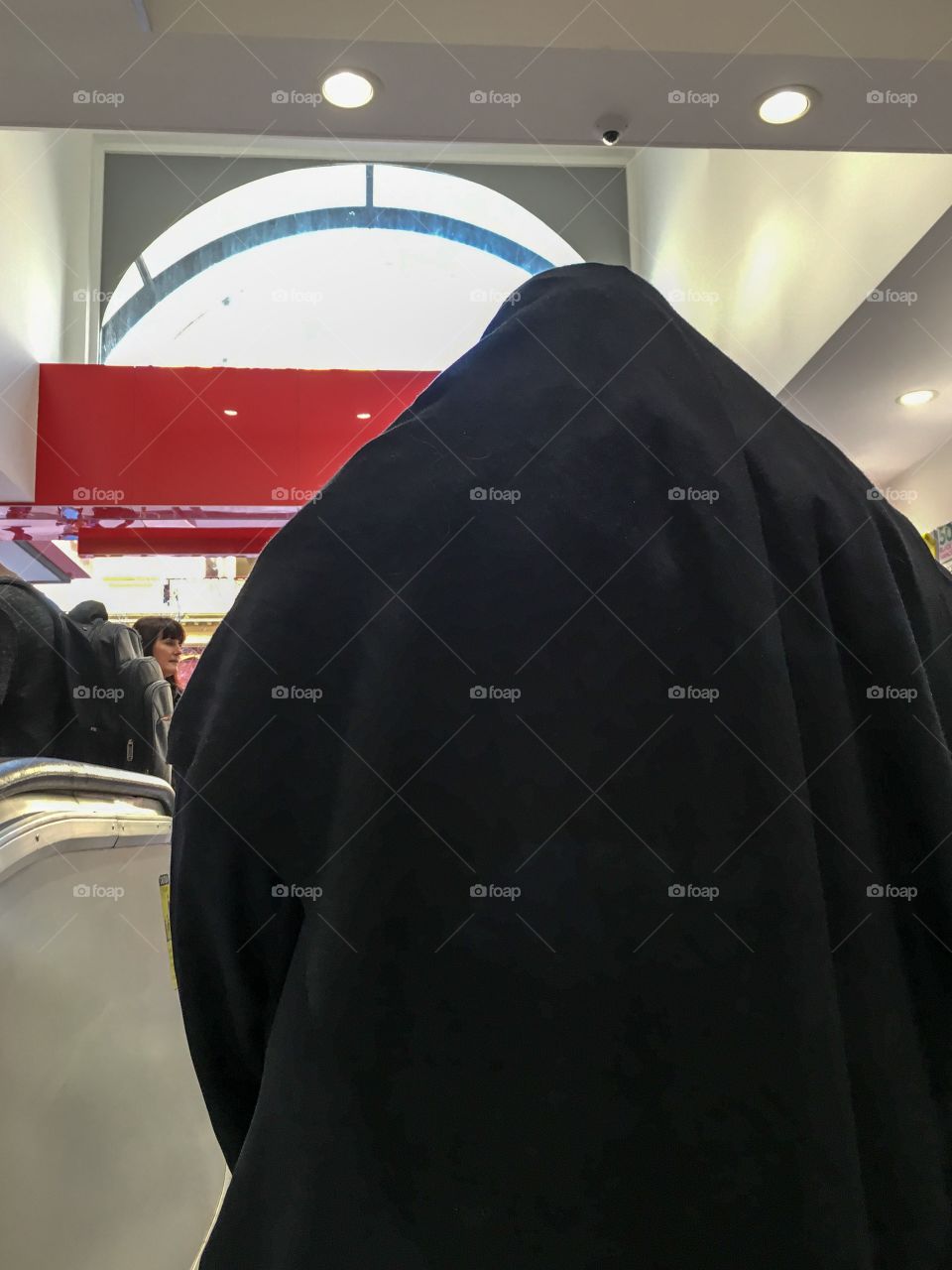 Muslim woman in black climbing escalator back view wearing hijab