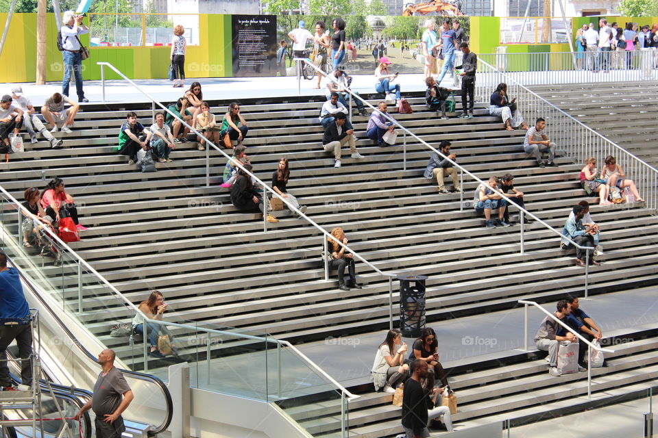 People are sitting on the stairs and hanging out with friends or co-workers in a open air shopping and business center in Paris