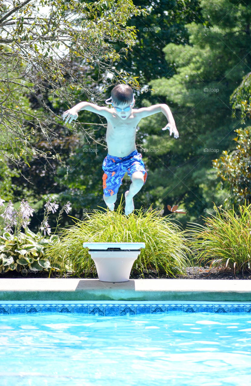 Young boy in the air after jumping off of a diving board above a dugout swimming pool