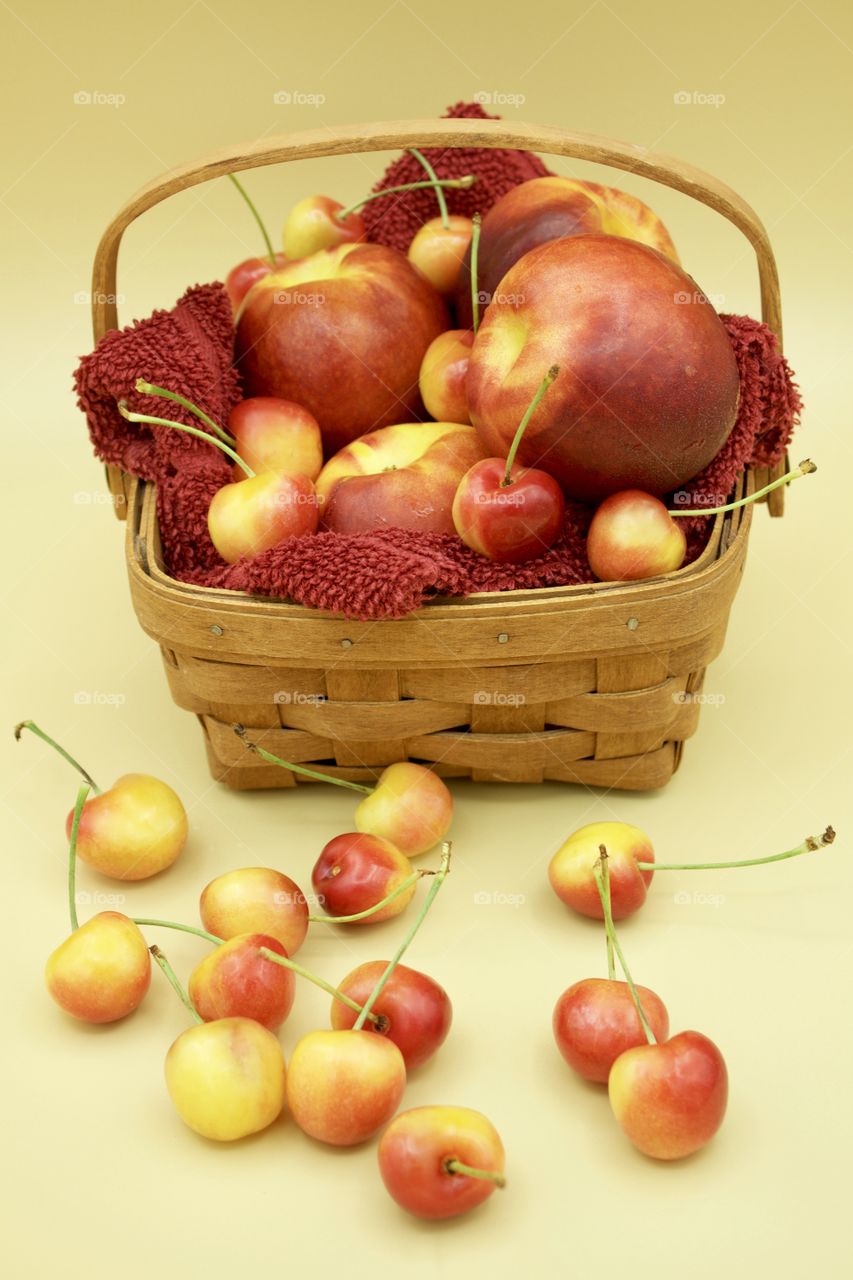 Fruits! - Nectarines And Rainer cherries in a wooden basket against a yellow background 