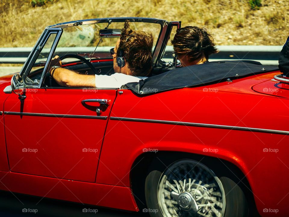 Beautiful vintage red car, with two young people, traveling to Spain for summer holiday.