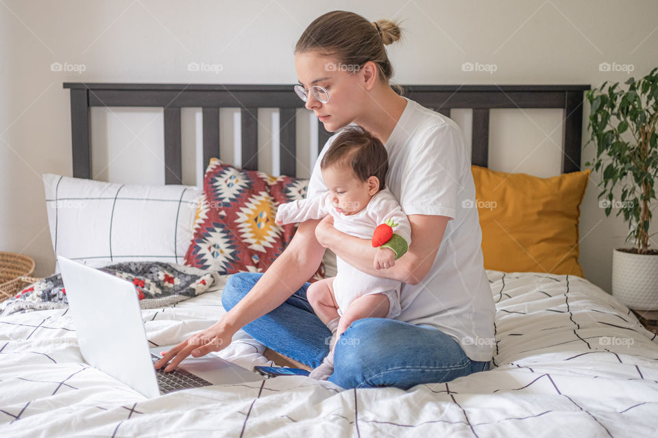 Young mother working from home on laptop spending time with baby