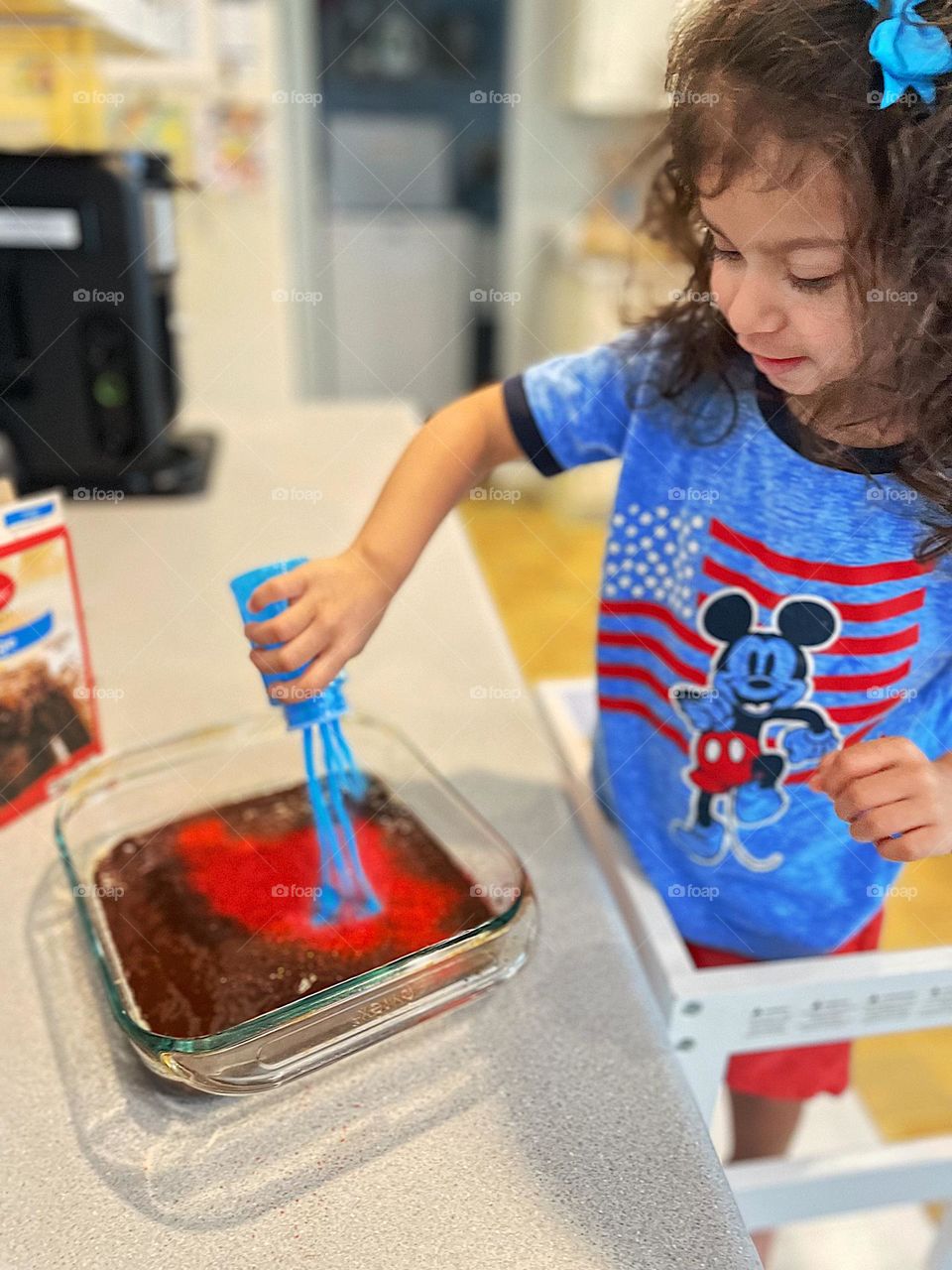 Toddler girl adds lots of blue and red sprinkles to brownies, making Independence Day desserts with children, making desserts for Fourth Of July party, having fun while making party desserts