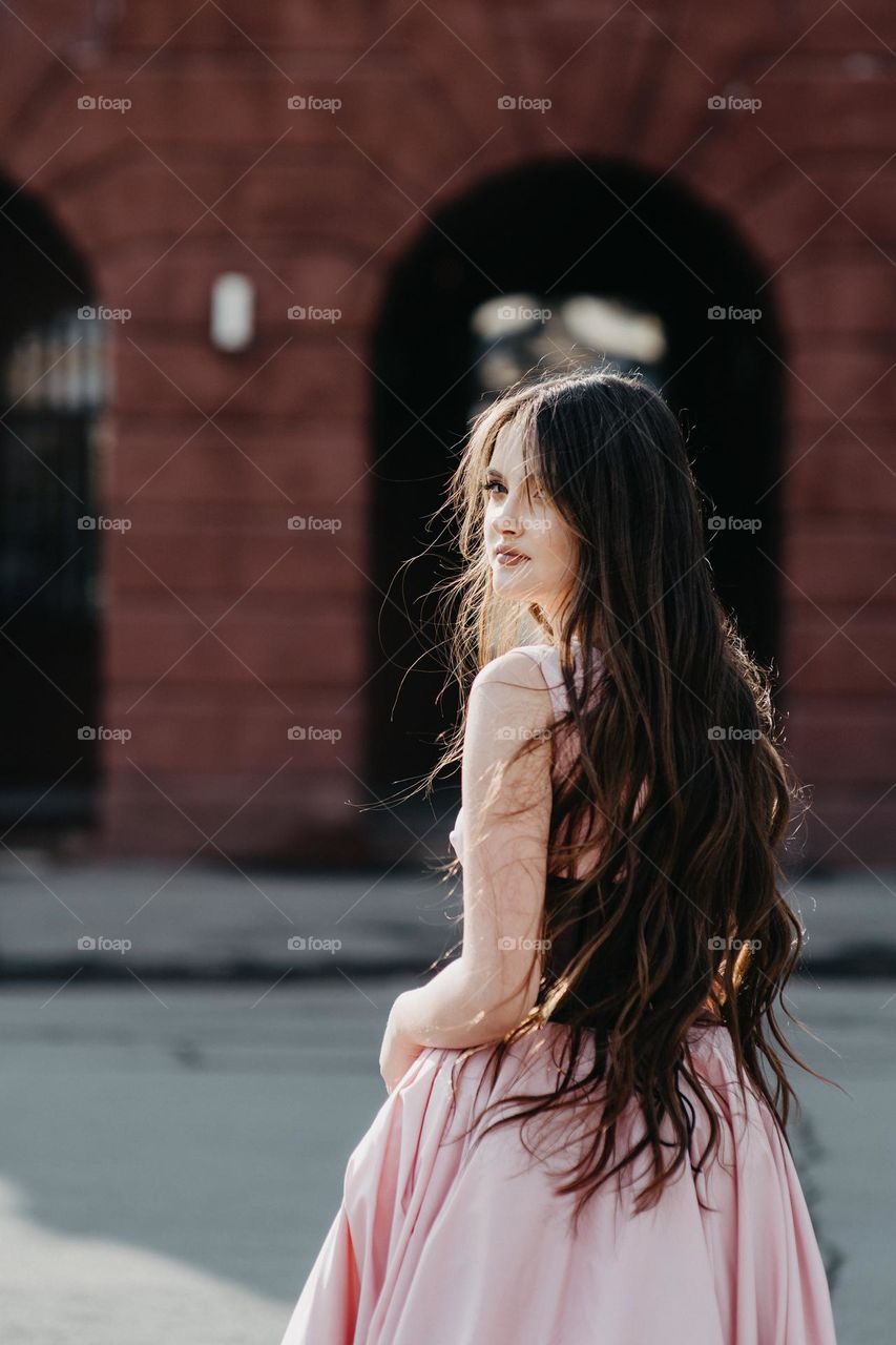 Portrait of beautiful girl in pink drress. Photo of woman with long hair from behind