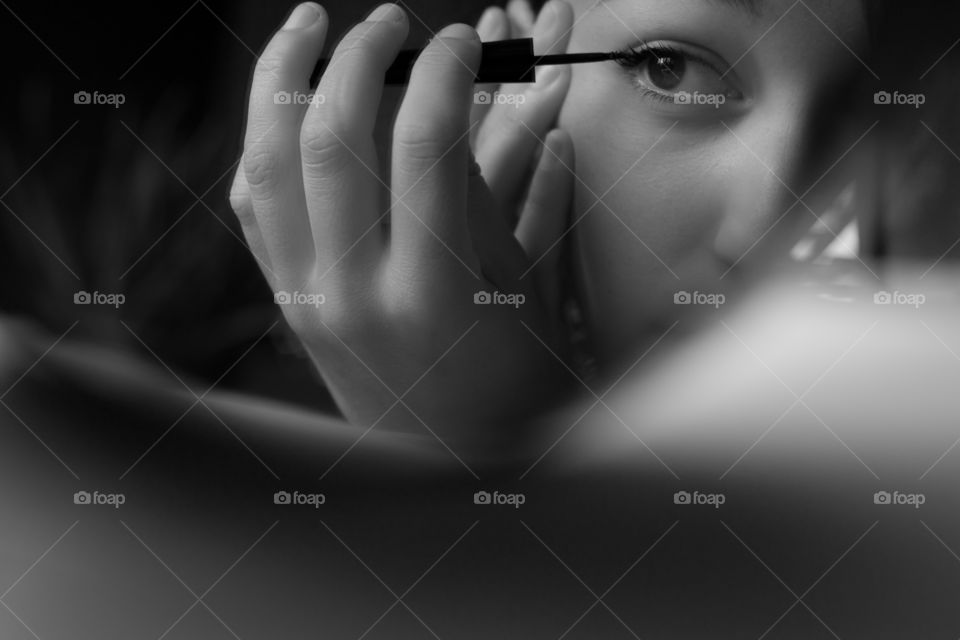 Young girl puts on makeup in front of the mirror. Black and white.