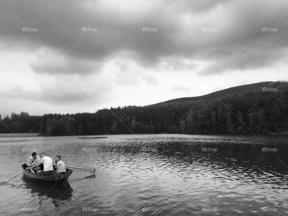 Black and white photograph of boat with people on a lake and storm clouds above